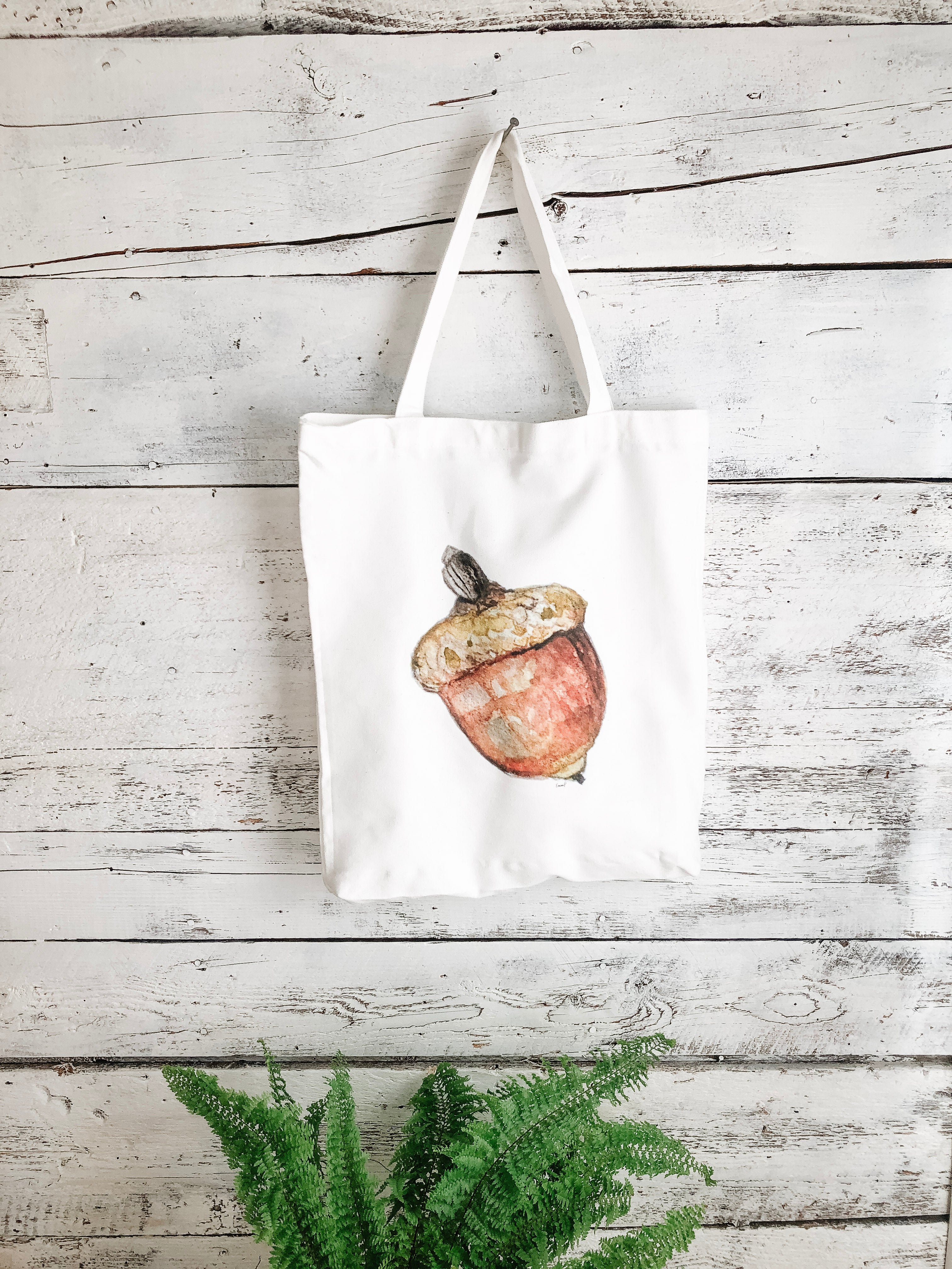 white canvas bag with painted brown acorn in the middle.  